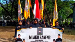 Calon warga perempuan PSHT Cabang Kota Kediri Pusat Madiun memegang spanduk acara Mlaku Bareng sambil membawa bendera merah putih dan atribut organisasi.