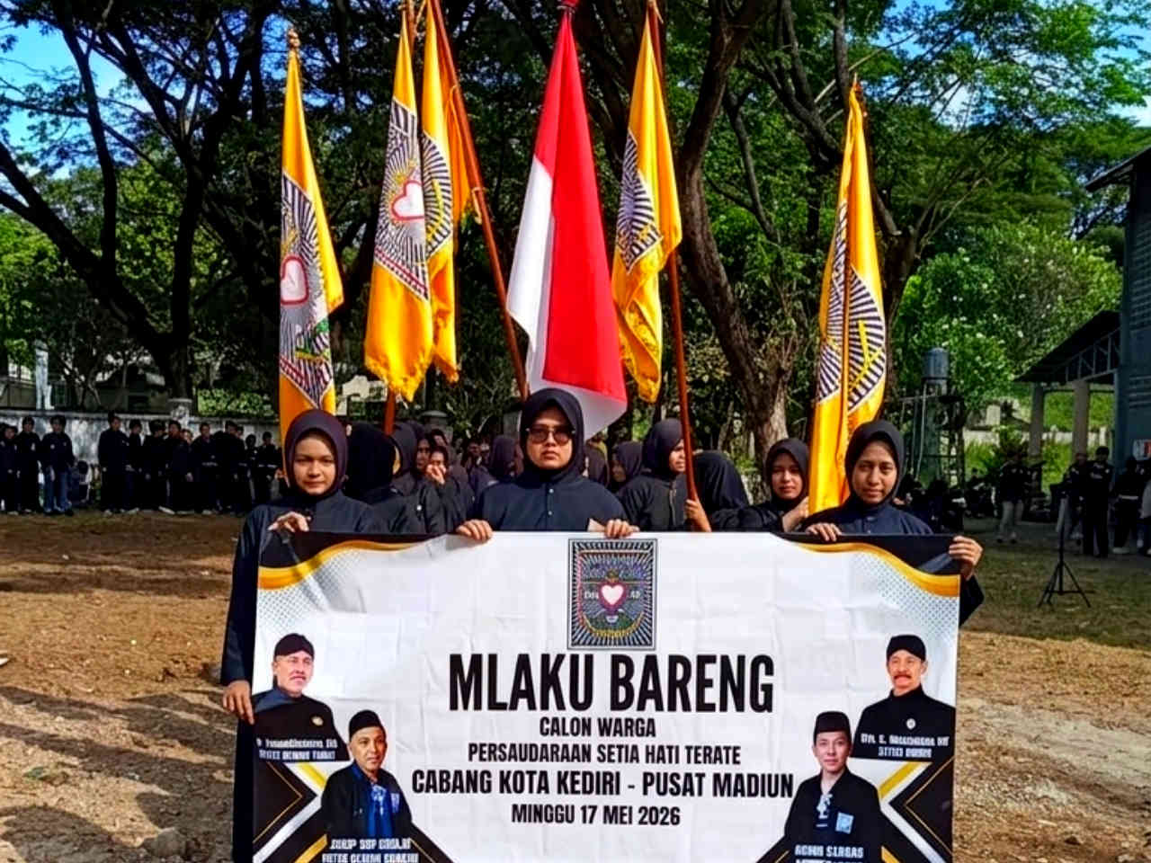 Calon warga perempuan PSHT Cabang Kota Kediri Pusat Madiun memegang spanduk acara Mlaku Bareng sambil membawa bendera merah putih dan atribut organisasi.