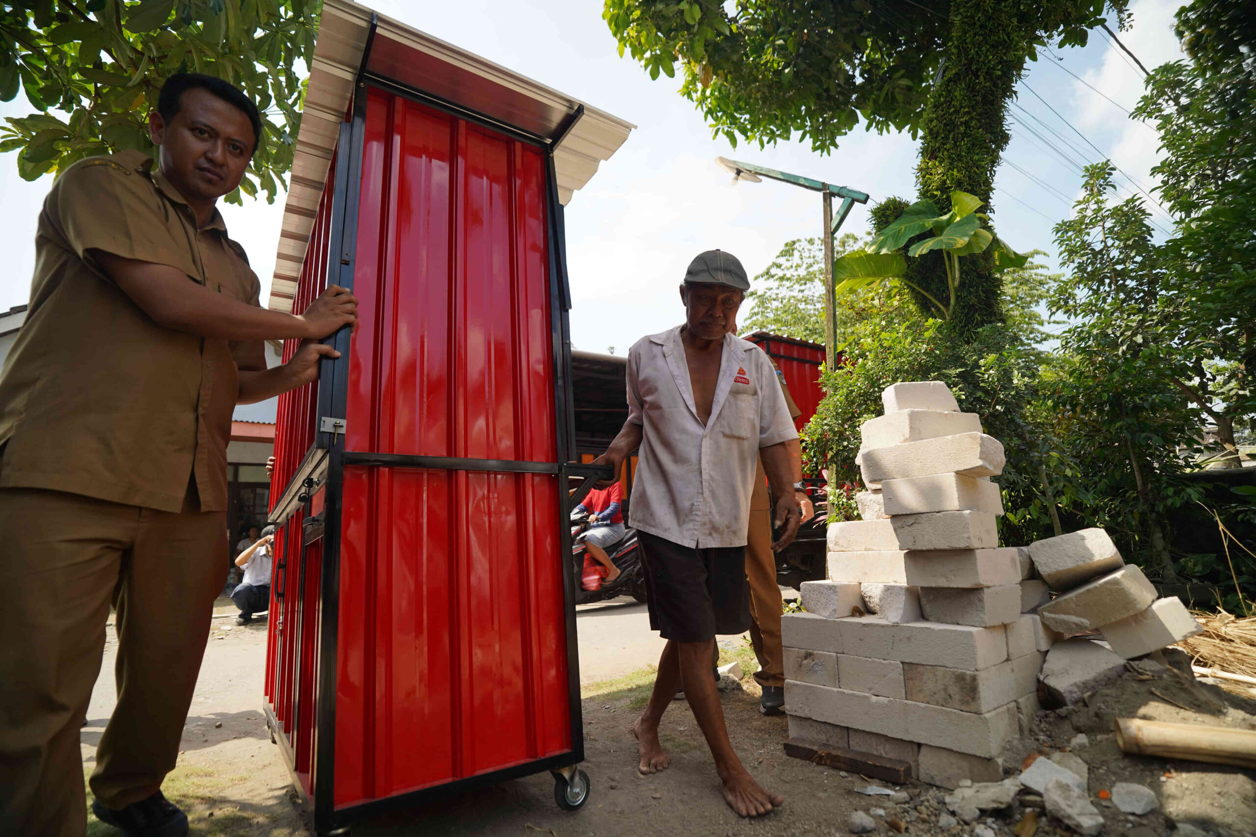 Mbah Mari bersama petugas Dinas Kopusmik Kabupaten Kediri memindahkan rombong kontainer merah bantuan dari Bupati Hanindhito Himawan Pramana (Mas Dhito) di Desa Manggis, Kecamatan Puncu.