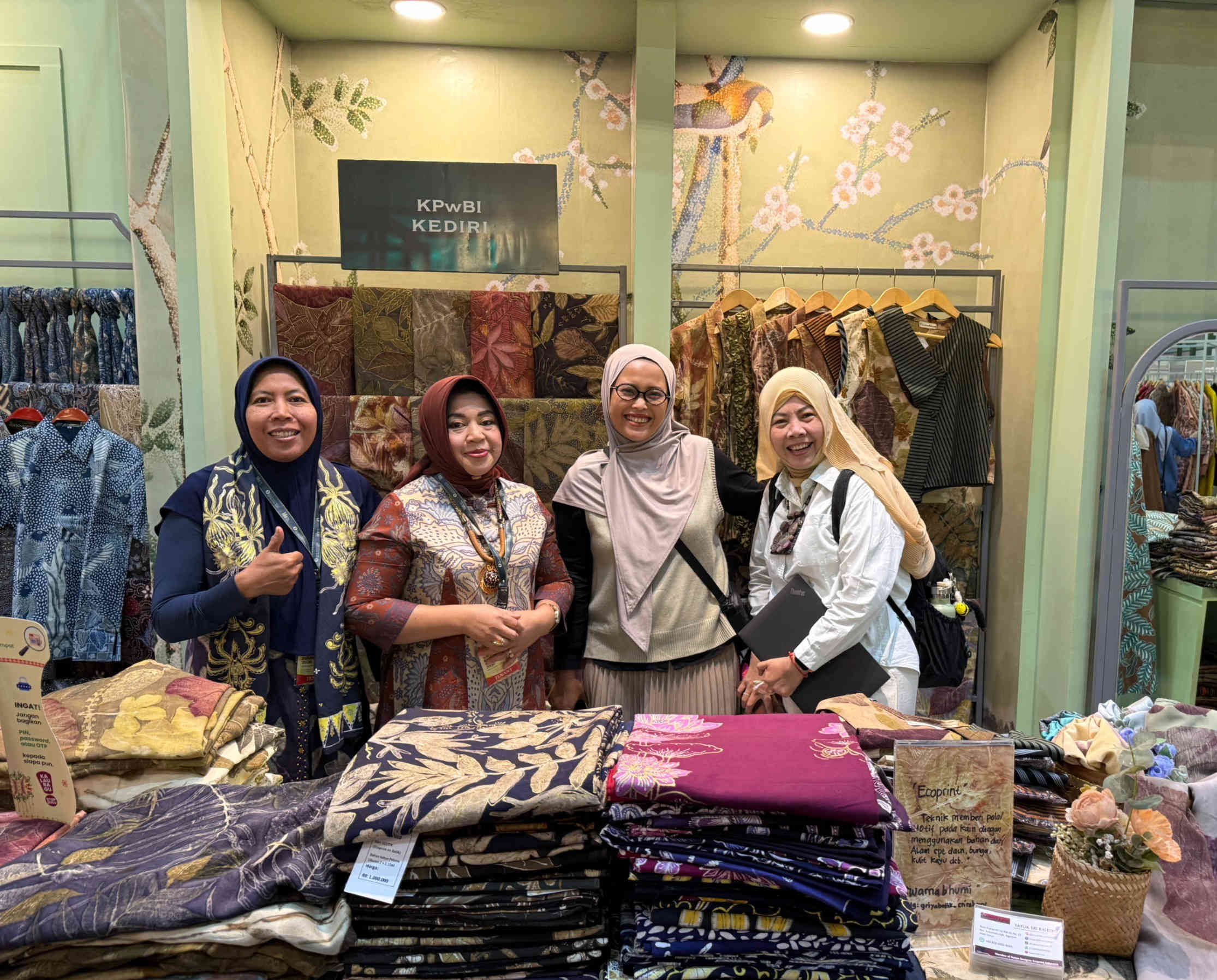 Empat wanita, termasuk perwakilan UMKM batik binaan KPwBI Kediri dan pejabat BI Kediri, tersenyum bangga di depan stan pameran penuh kain batik dan ecoprint berkualitas.