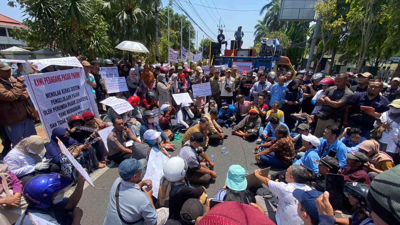 Ratusan pedagang pasar tradisional di Kota Kediri membentangkan spanduk tuntutan saat menggelar aksi duduk di jalan.